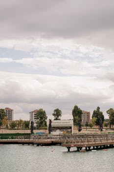 A serene urban waterfront scene featuring a pier and buildings under a cloudy sky.