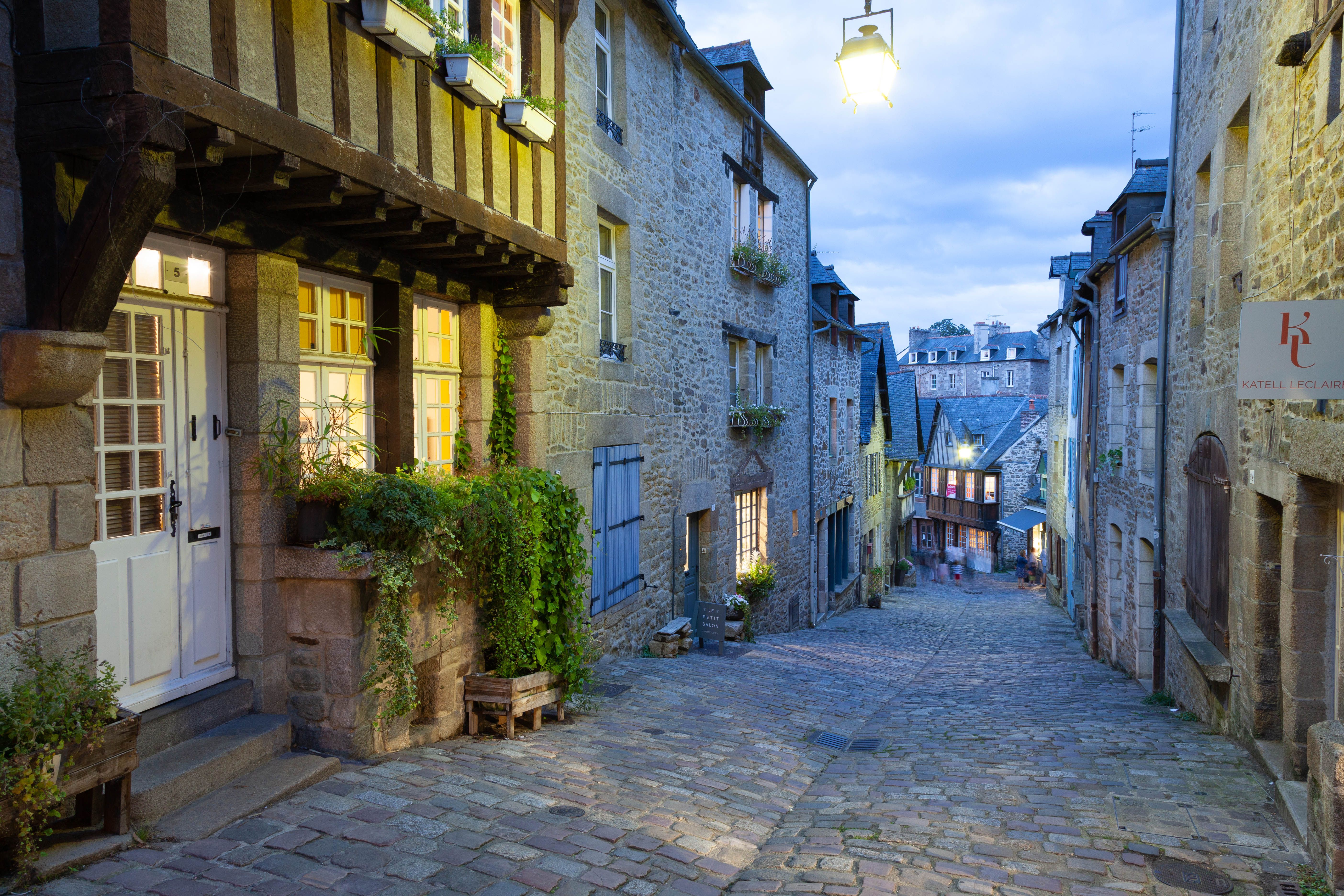 Explore the illuminated cobblestone streets of historic Dinan, Brittany at dusk.
