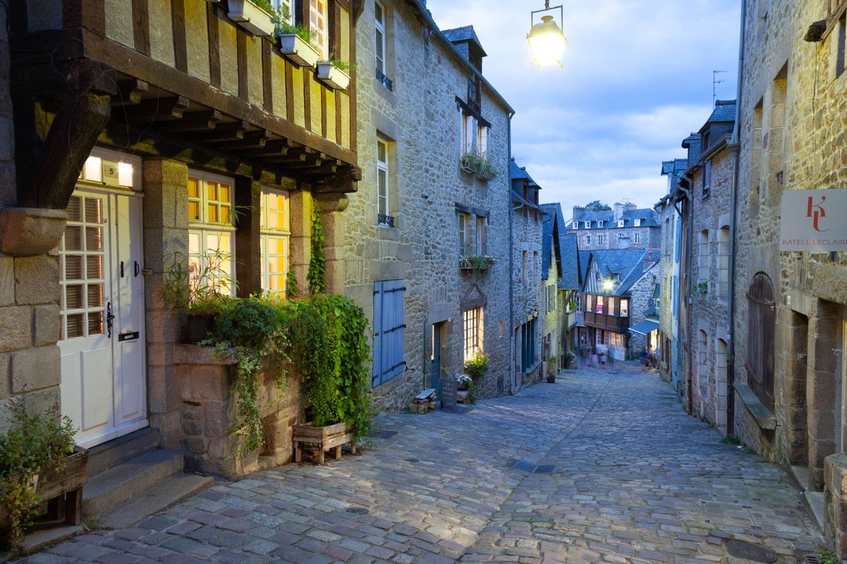 A Dinan cobblestone street at dusk, half-timbered windows lit