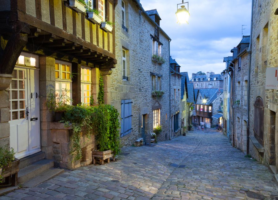 Explore the illuminated cobblestone streets of historic Dinan, Brittany at dusk.
