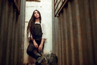 都市小巷里，一位穿着破旧工作服、头发飘逸的年轻女子，展现出时尚风格