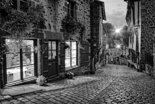 Free Black and white photo of a narrow cobblestone street in Dinan, Brittany, France, with historic buildings. Stock Photo