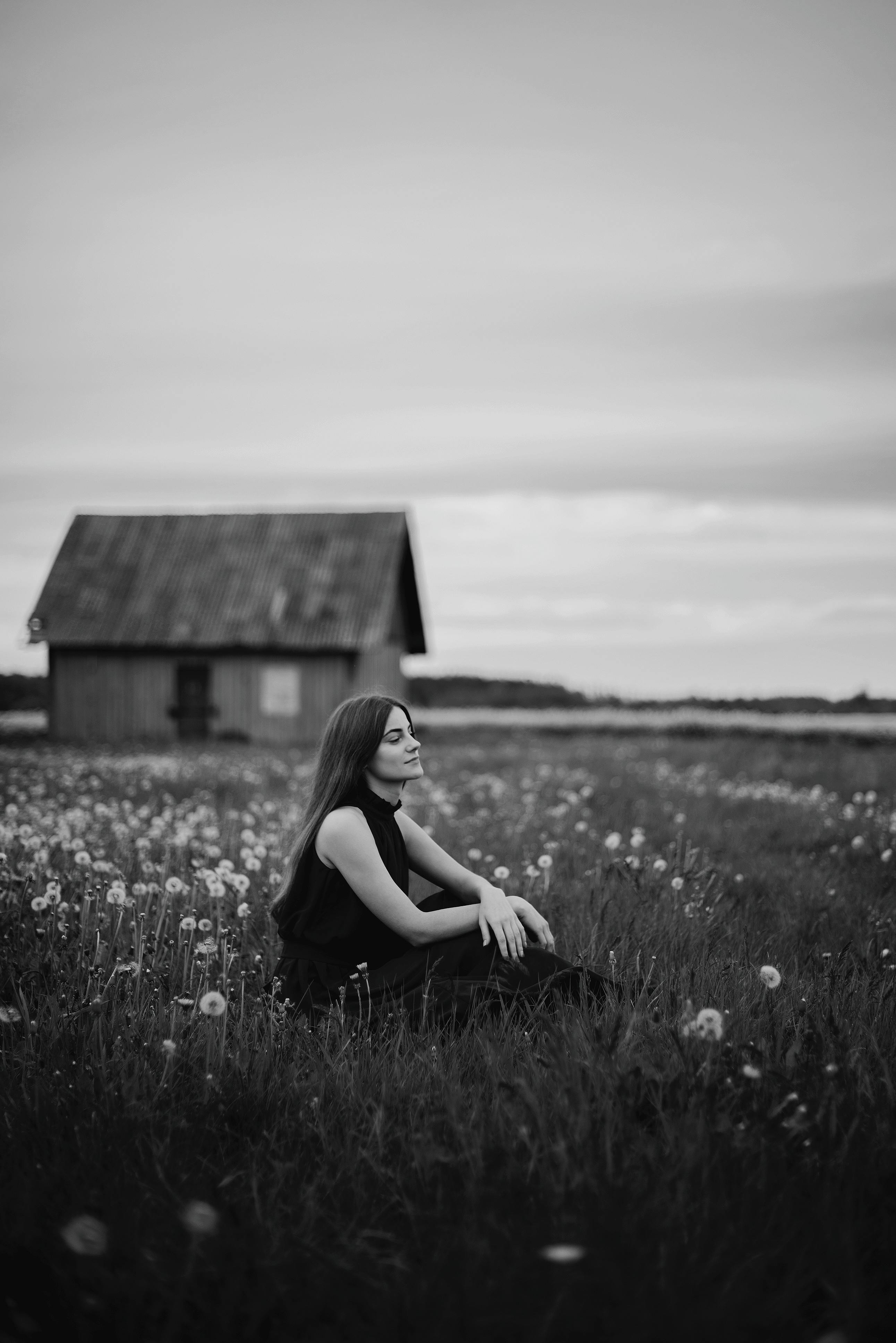Tranquil scene of a woman sitting in a meadow near a cottage in Kaunas, Lithuania.