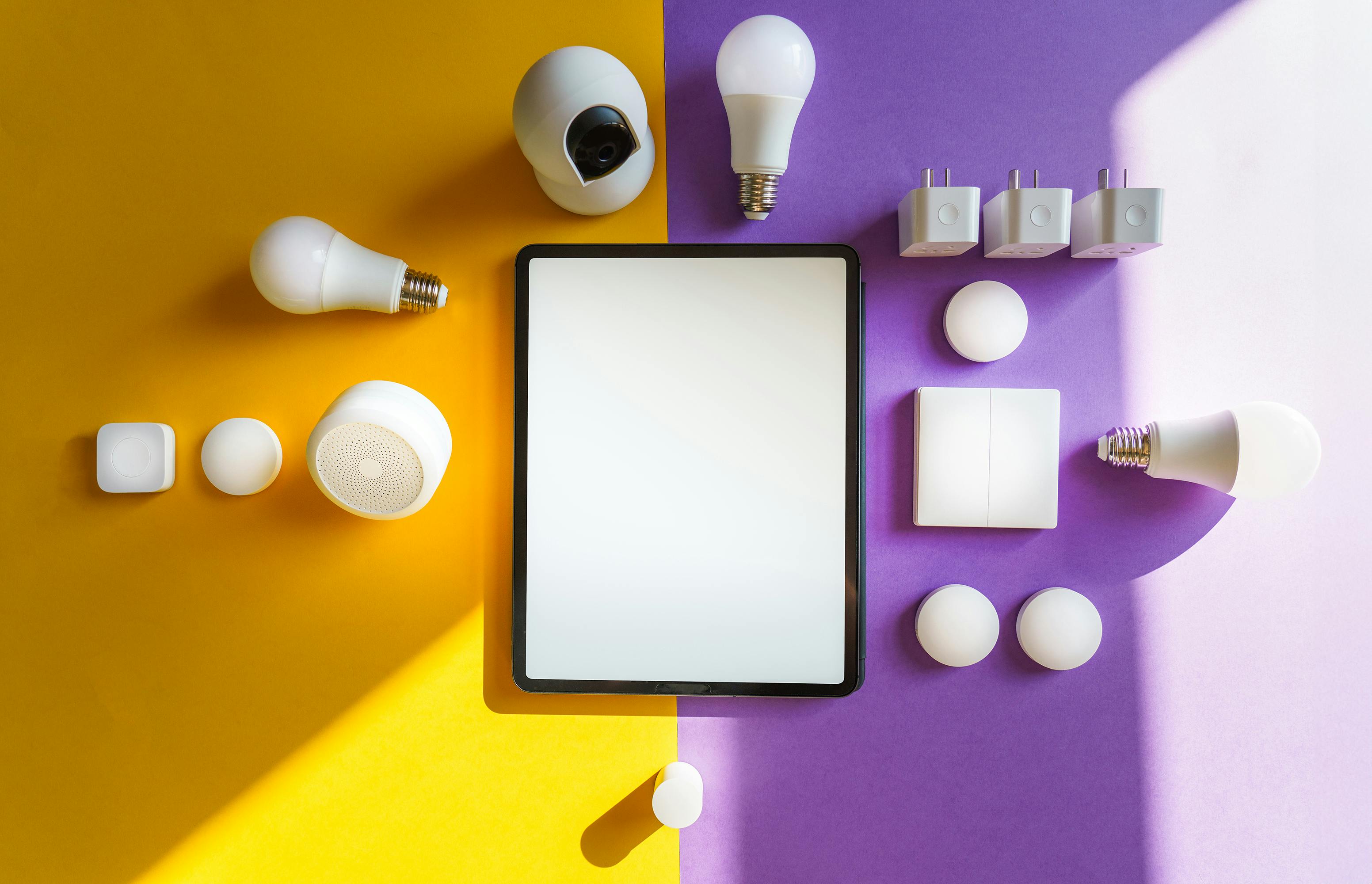 Top view of smart home devices and tablet on split yellow and purple background.