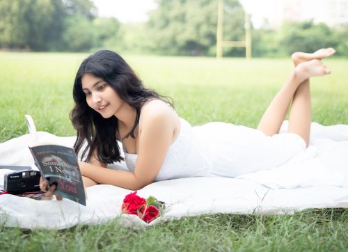 Free Young woman in white dress reading a book on a picnic blanket outdoors with roses. Stock Photo