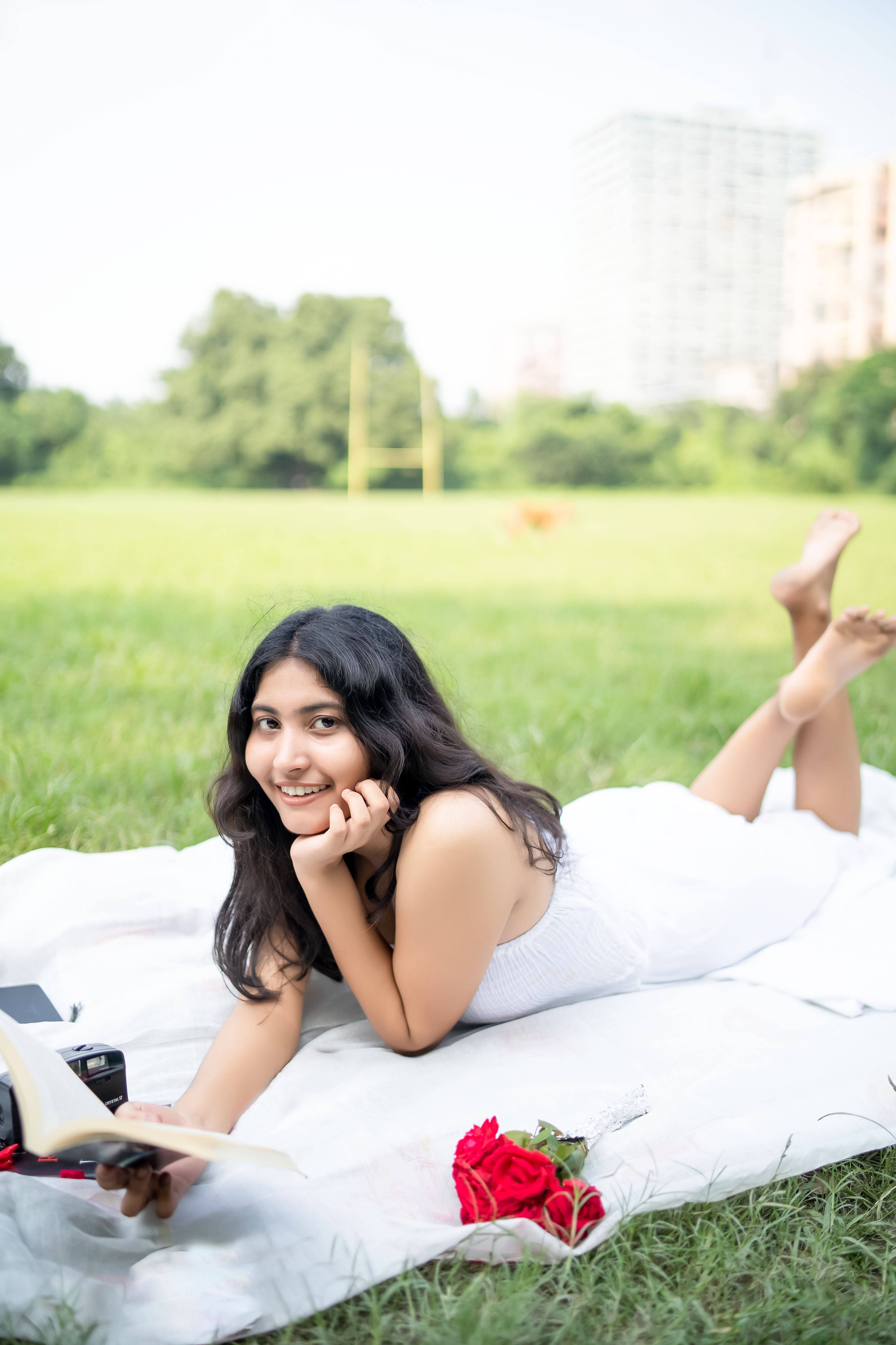 Young woman in white dress reading a book during a picnic in a green park.