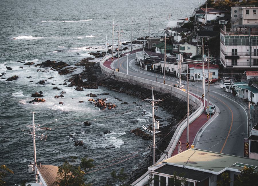 Aerial view of a coastal road and town in Gangneung, South Korea, showcasing seaside urban landscape.