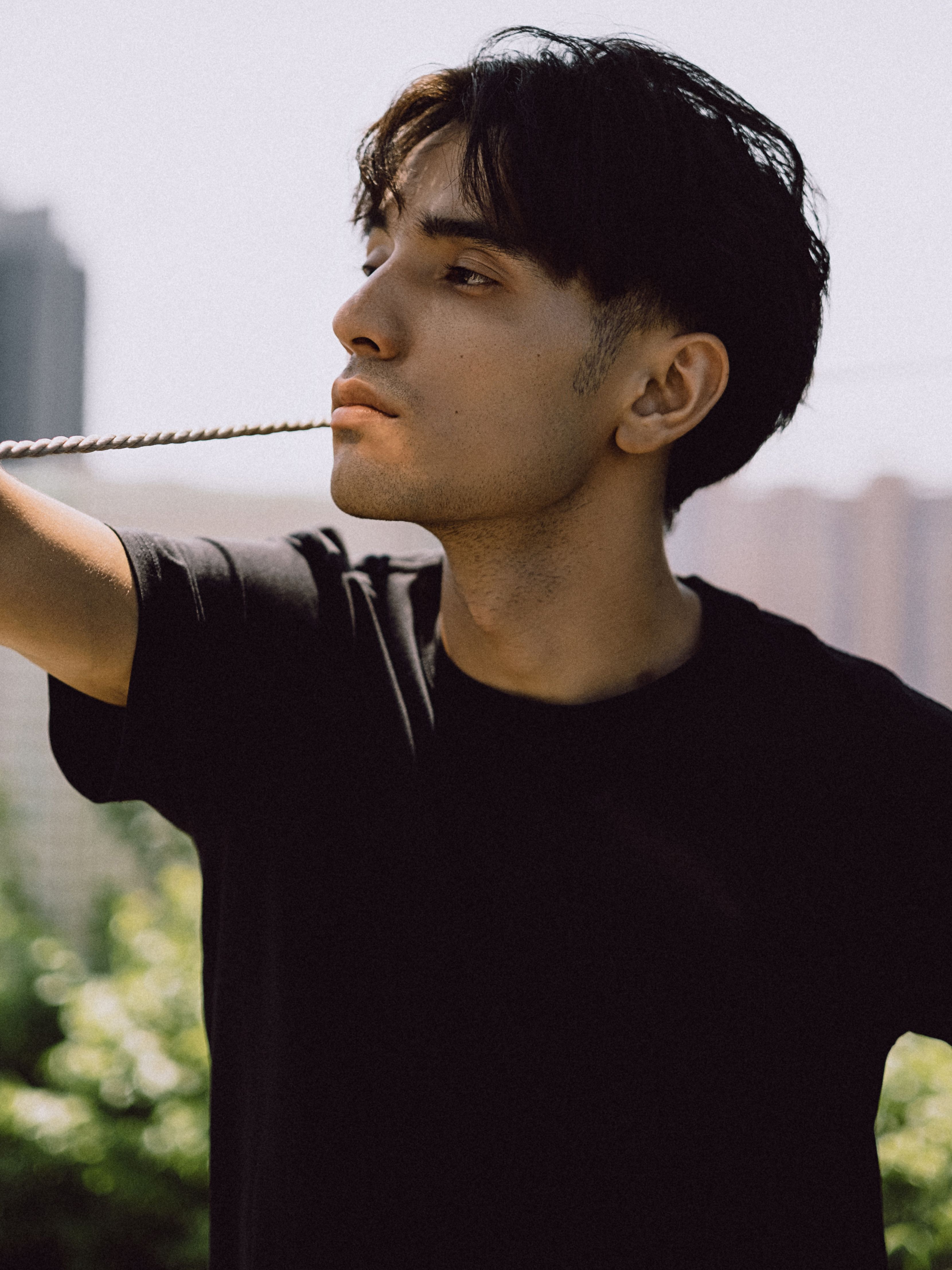 Portrait of a young man in a black t-shirt against an outdoor urban backdrop with greenery.