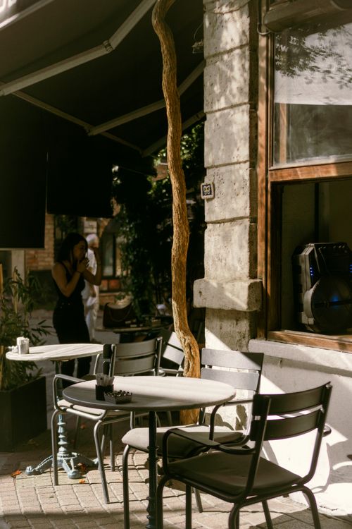 Free Charming outdoor cafe scene with empty tables and chairs on a shaded city street. Stock Photo