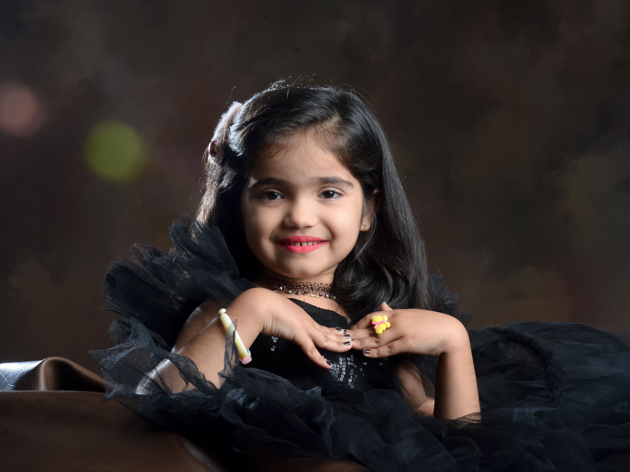 A delightful portrait of a young girl in a black dress, smiling gently in a studio.