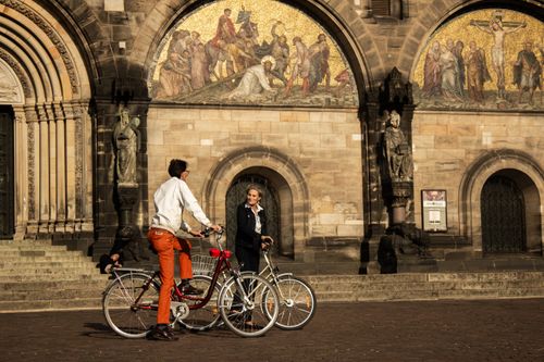 Free Two cyclists ride in front of the ornate arches of Bremen Cathedral, Germany. Stock Photo