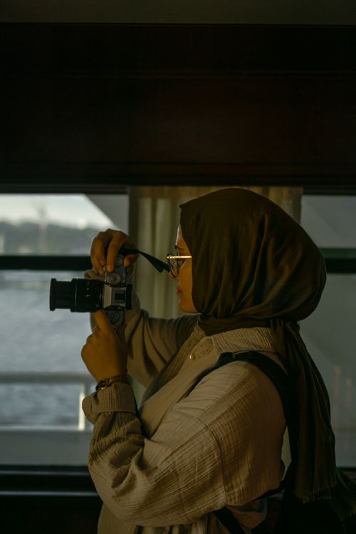 Free Young muslim woman in hijab taking photos with camera indoors, side view Stock Photo