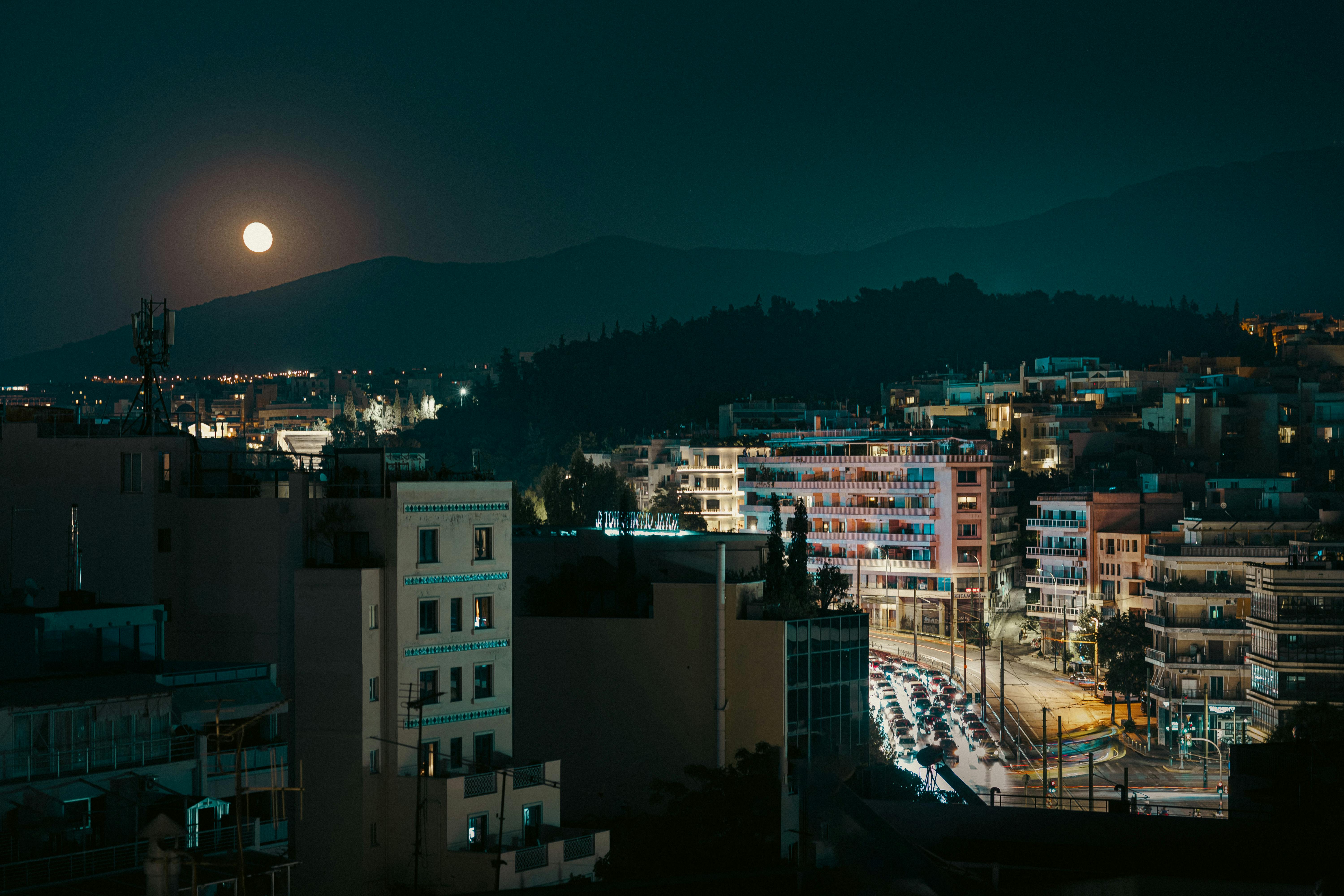 Urban Athens skyline illuminated by streetlights under a full moon at night.