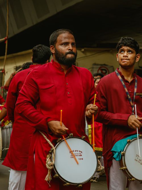 Free Men in red attire playing drums during a cultural parade on Mumbai streets. Stock Photo