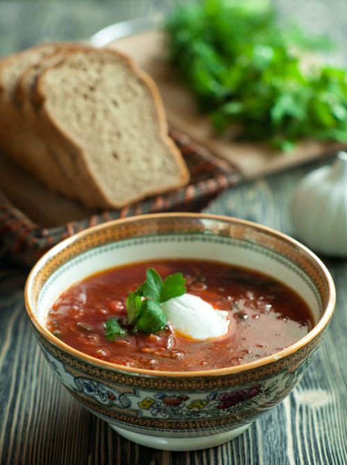 Free Close-up of a bowl of borscht soup with sour cream and herbs on a wooden table, served with bread. Stock Photo
