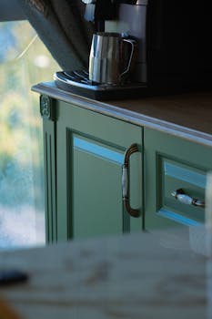 Close-up of a stylish green cabinet with a coffee maker on top, in a kitchen setting.
