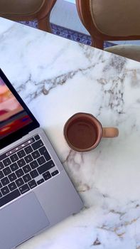 Top view of a laptop and a coffee mug on a marble table, perfect for work or study time.