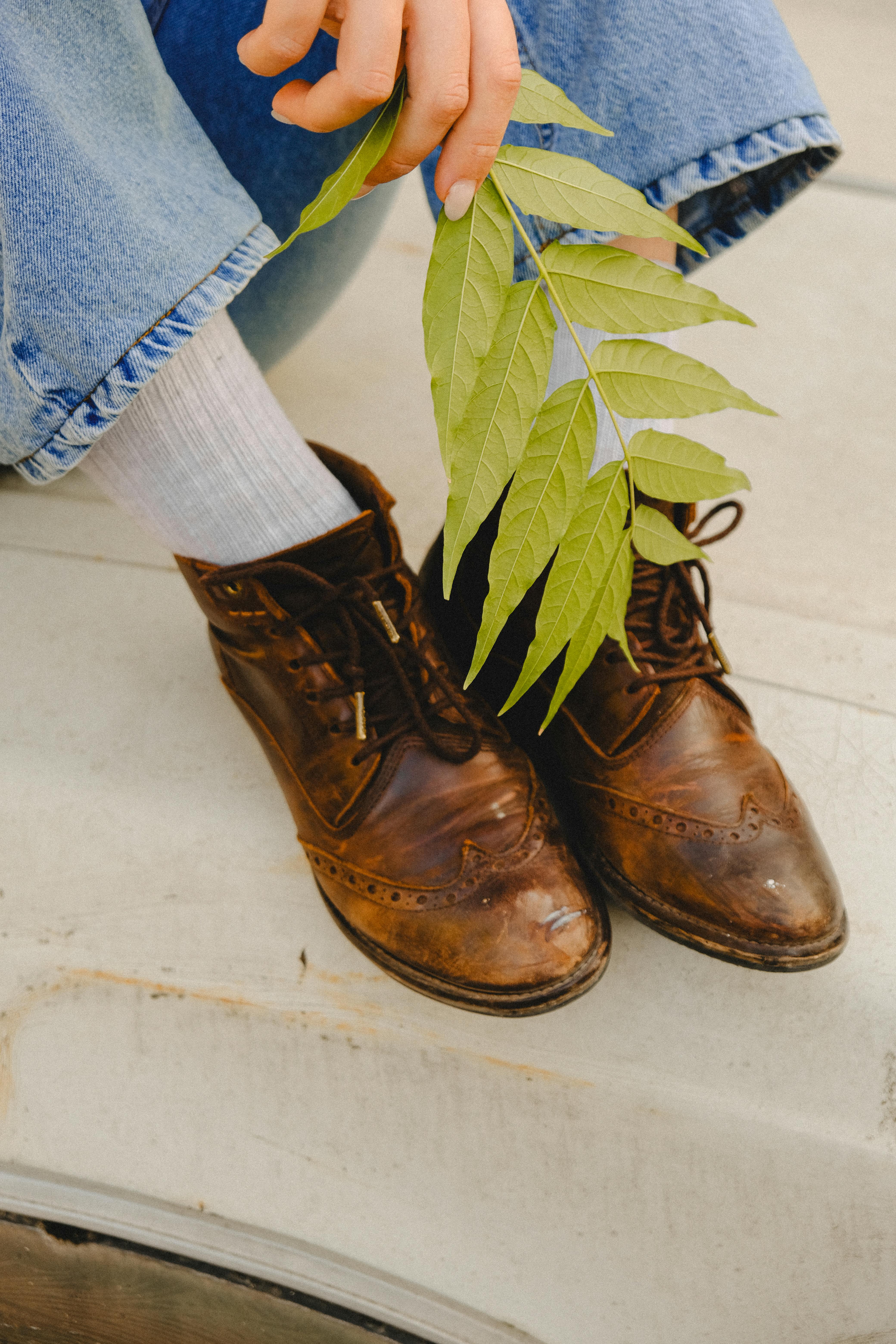 Rustic leather shoes paired with green leaves and denim, creating a vintage aesthetic.