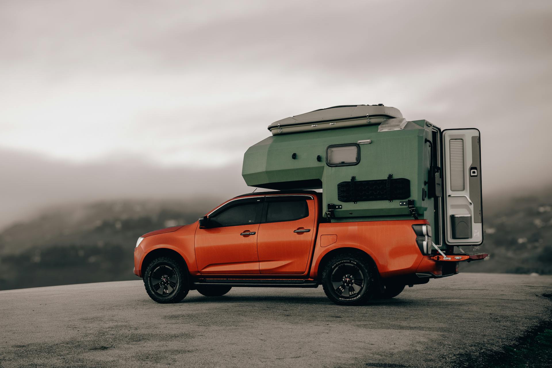A vibrant orange pickup truck with a green camper stands on a mountain road in foggy Ordu, Türkiye.