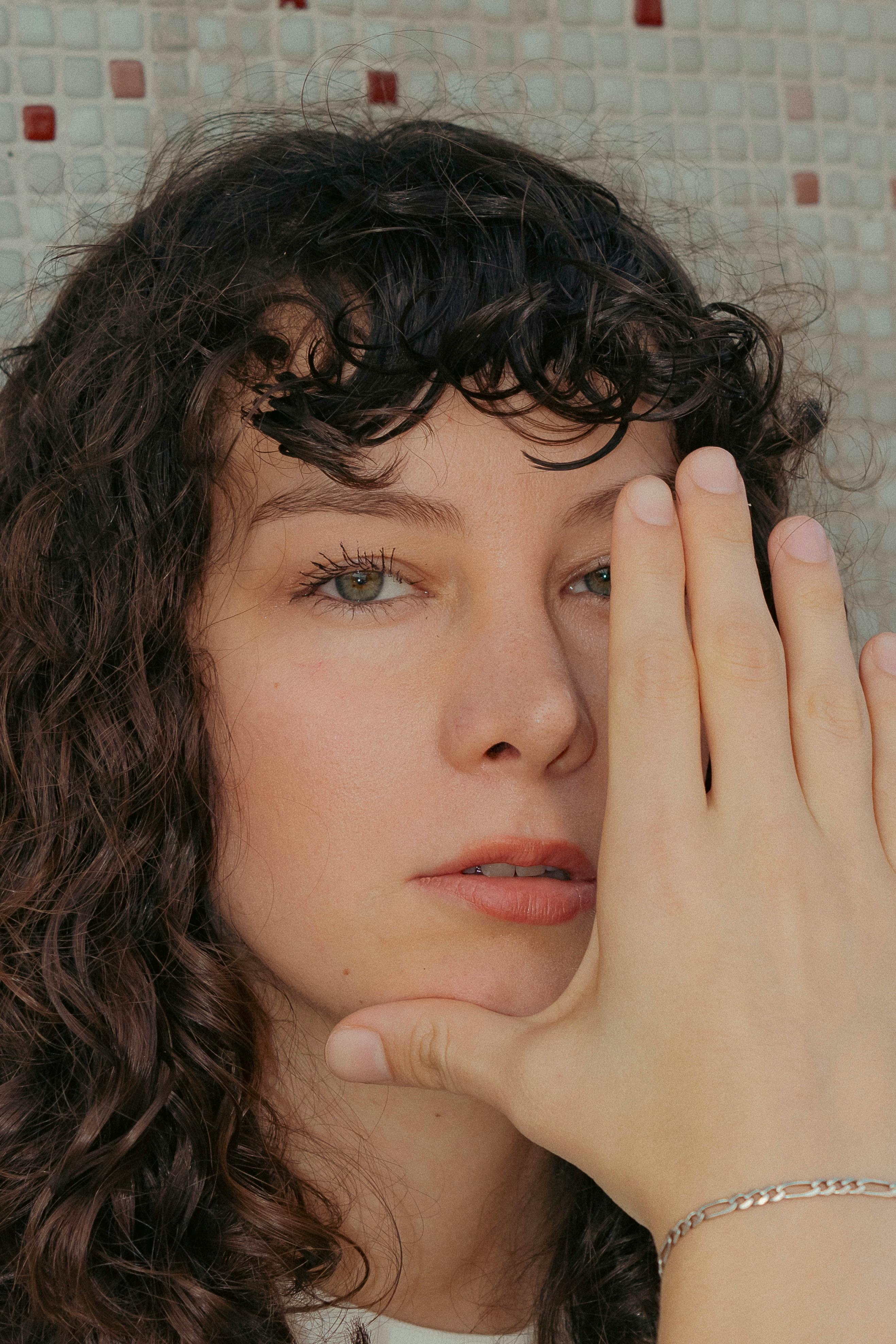 Close-up portrait of a woman with curly hair covering her face with her hand.