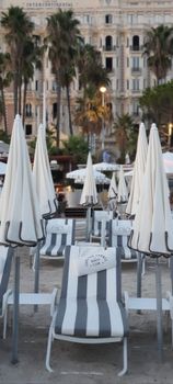 Chic striped sun loungers with closed umbrellas on a serene beach near a luxury hotel.