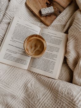 Warm and inviting scene of a cappuccino with an open book on a cozy textured blanket.