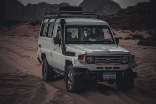 Free Explore the rugged terrain of Egypt with a white jeep navigating a dusty desert path. Stock Photo