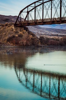 一座质朴的金属桥倒映在平静的河面上，四周环绕着宁静的自然景色