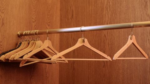 A row of wooden hangers on a metal rod in an empty, wood-paneled closet.
