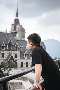 Person observing ornate castle architecture under cloudy skies.