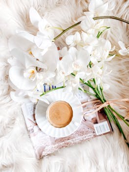 Top view of coffee and white orchids on fluffy rug, creating a serene morning vibe.