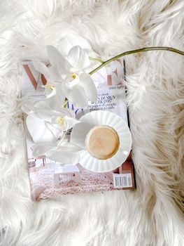 Stylish coffee setting with white orchids and a magazine on plush fabric.