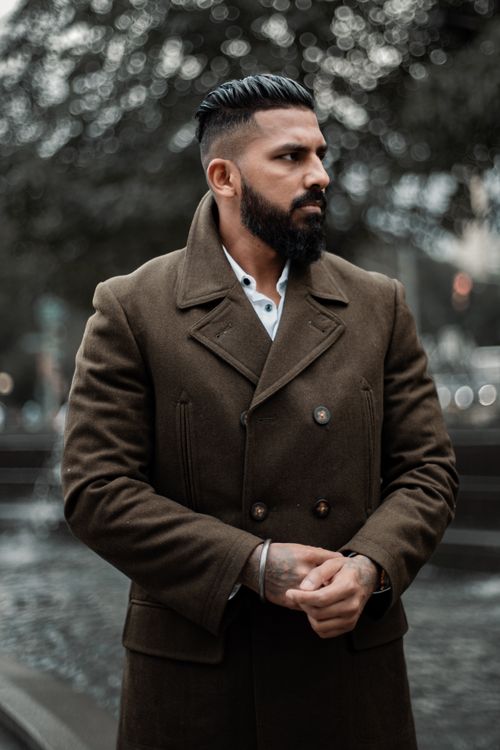 Free Fashionable man with beard posing in a brown overcoat in an urban outdoor setting. Stock Photo
