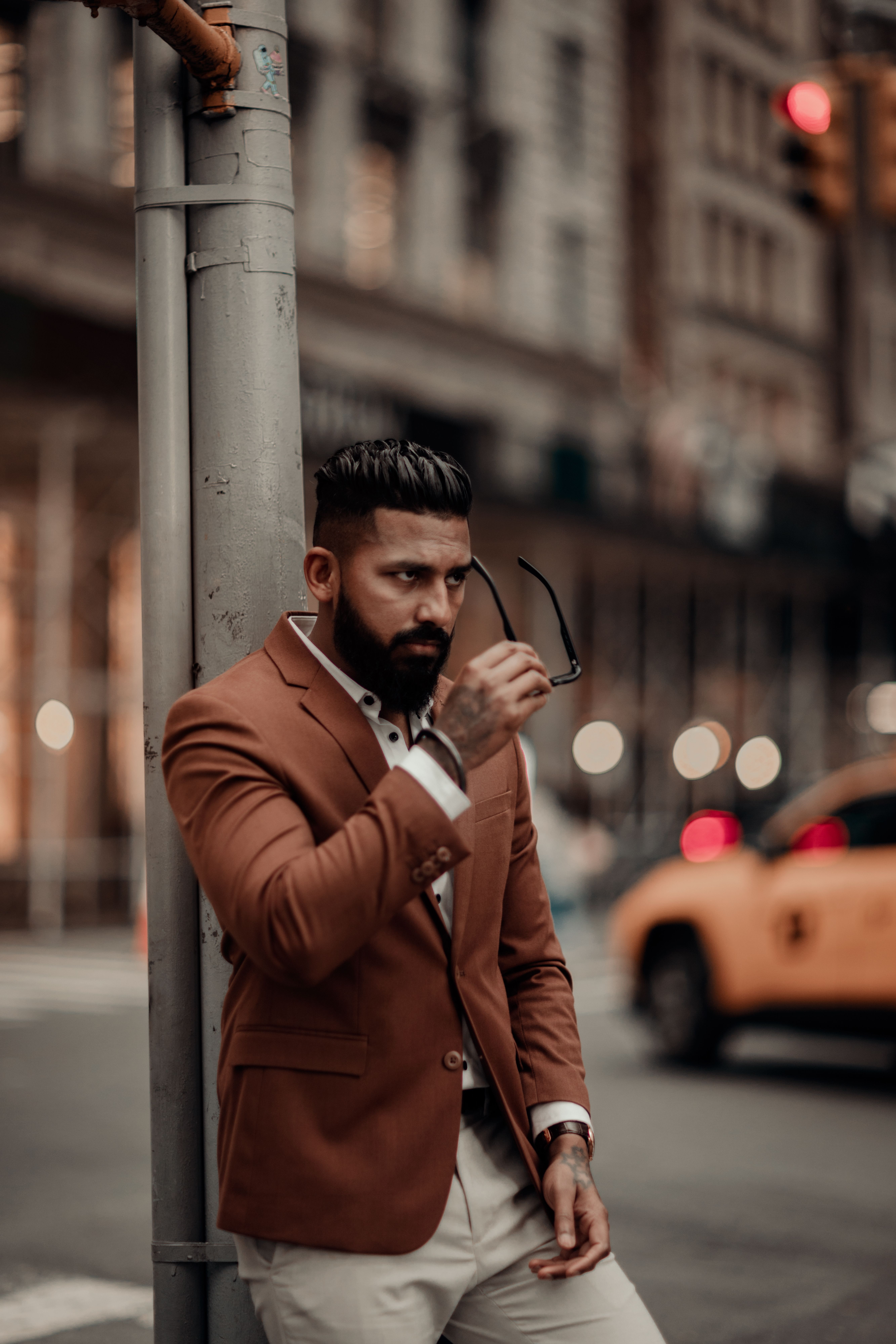 Stylish man in brown blazer poses confidently on urban city street.