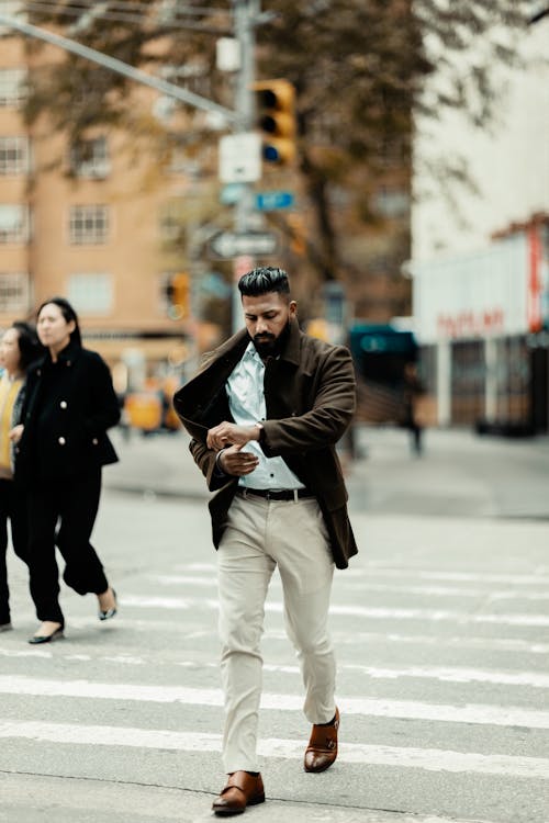 Man in a Brown Coat and White Shirt Looking at his Watch while Crossing the Road