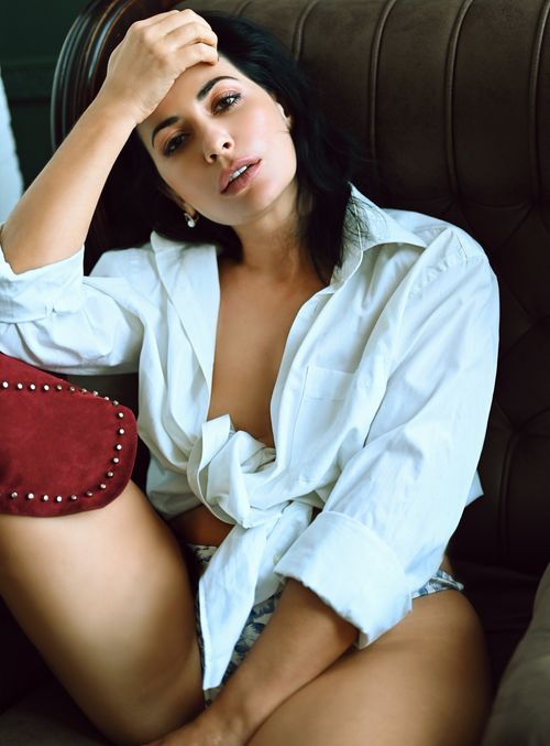 Free A stylish woman sits on a chair posing in a white blouse, showcasing modern fashion. Stock Photo