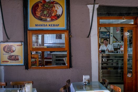 Cozy indoor view of a Turkish restaurant with Manisa kebab posters and a waiter at the counter.