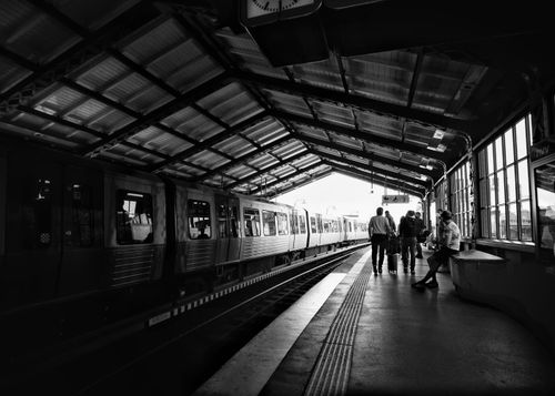 Free A moody black and white photograph of people waiting at a train station platform. Stock Photo