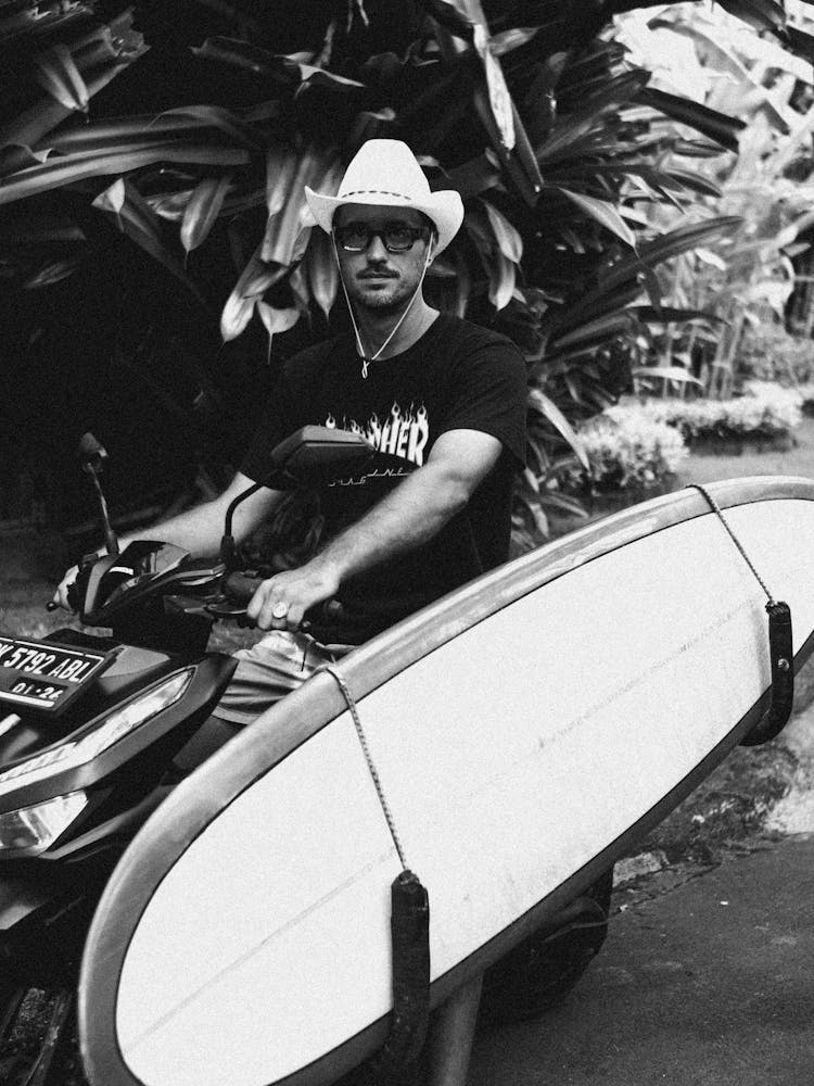 Man In Hat And With Surfboard On Motor Scooter