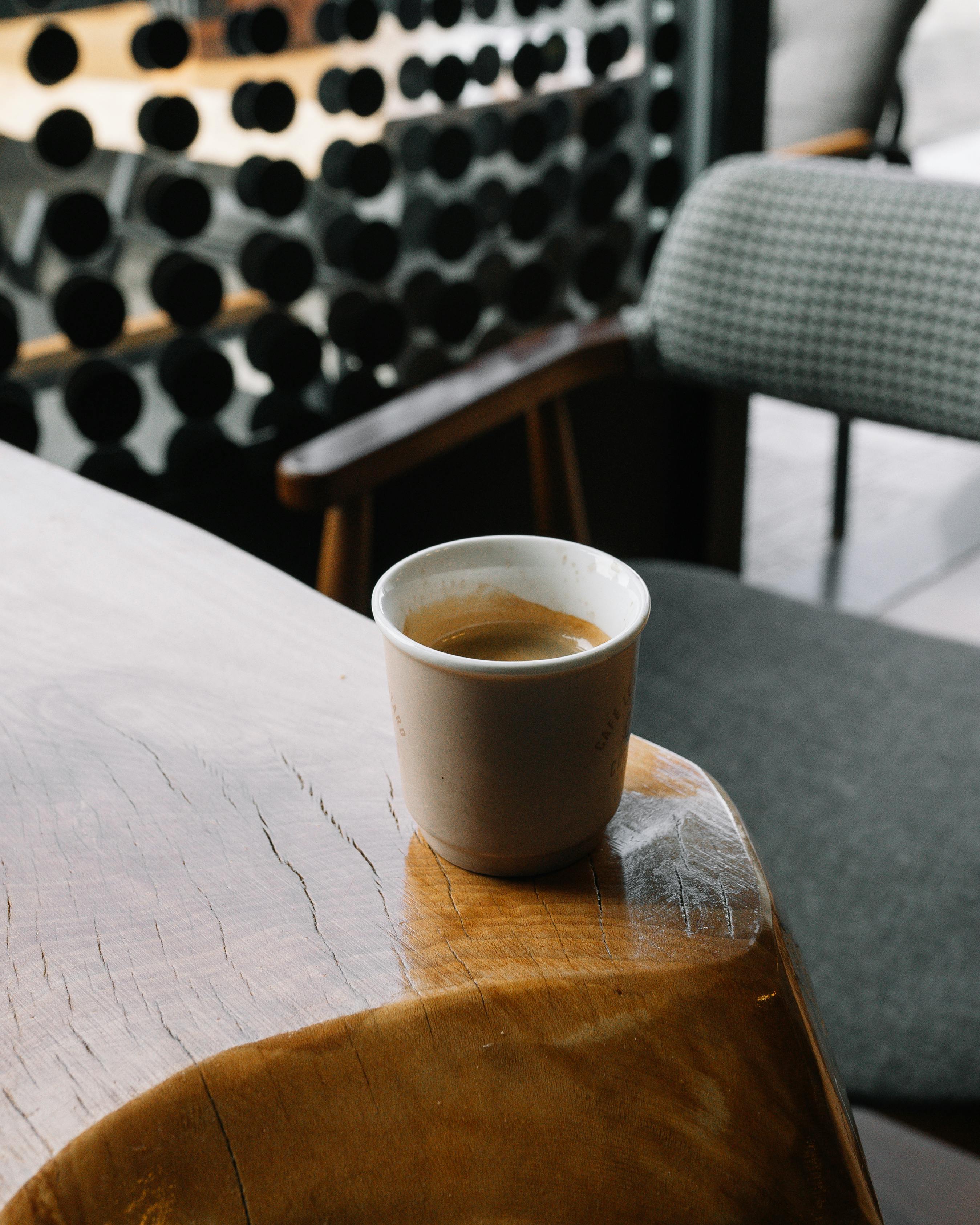 A cozy indoor café setting featuring a steaming cup of coffee on a wooden table with chairs in the background.
