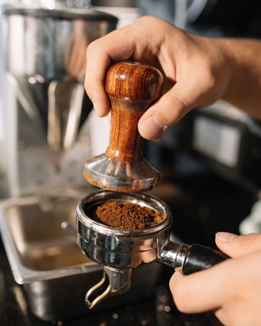 A barista using a tamper to prepare ground coffee in a portafilter, perfect for espresso enthusiasts.