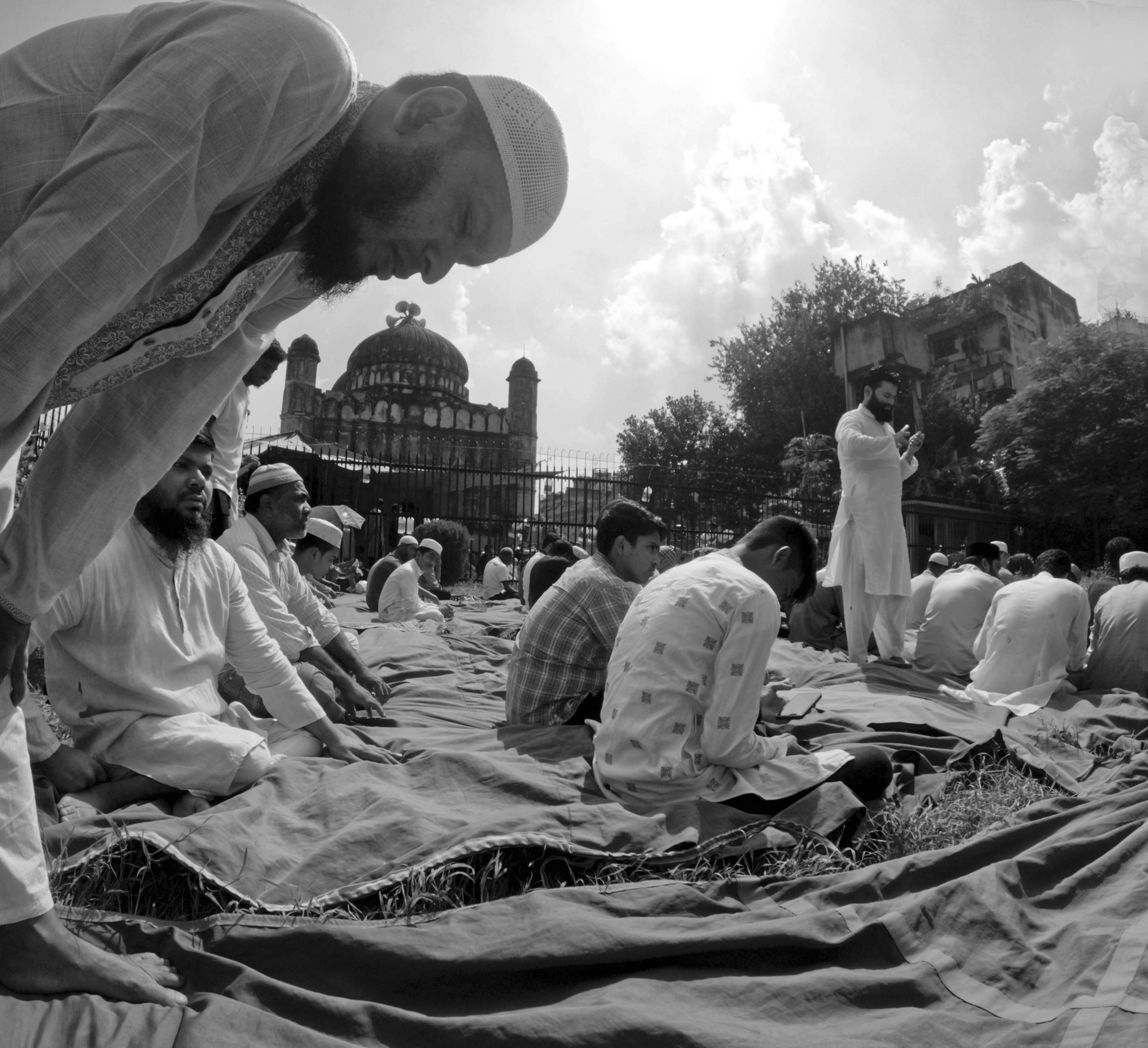 Muslim men gathered in Dhaka for outdoor communal prayer in a monochrome setting.