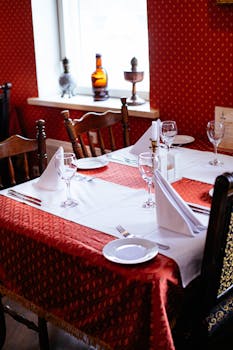 Chic table setup with red tablecloth, glassware, and napkins in a warm-toned restaurant.