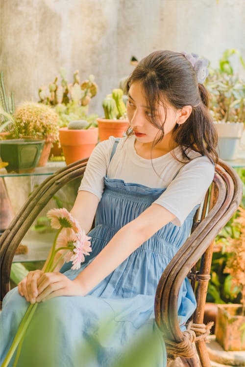 Young Woman Sitting among Plants and Holding Flowers