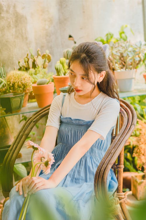 Young Woman Sitting among Plants and Holding Flowers