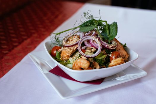 A delicious seafood salad featuring shrimp and salmon, topped with fresh greens and red onions.