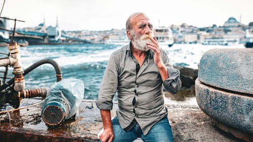 Elderly Man with a Gray Beard Sitting on the Shore in Istanbul, Turkey 