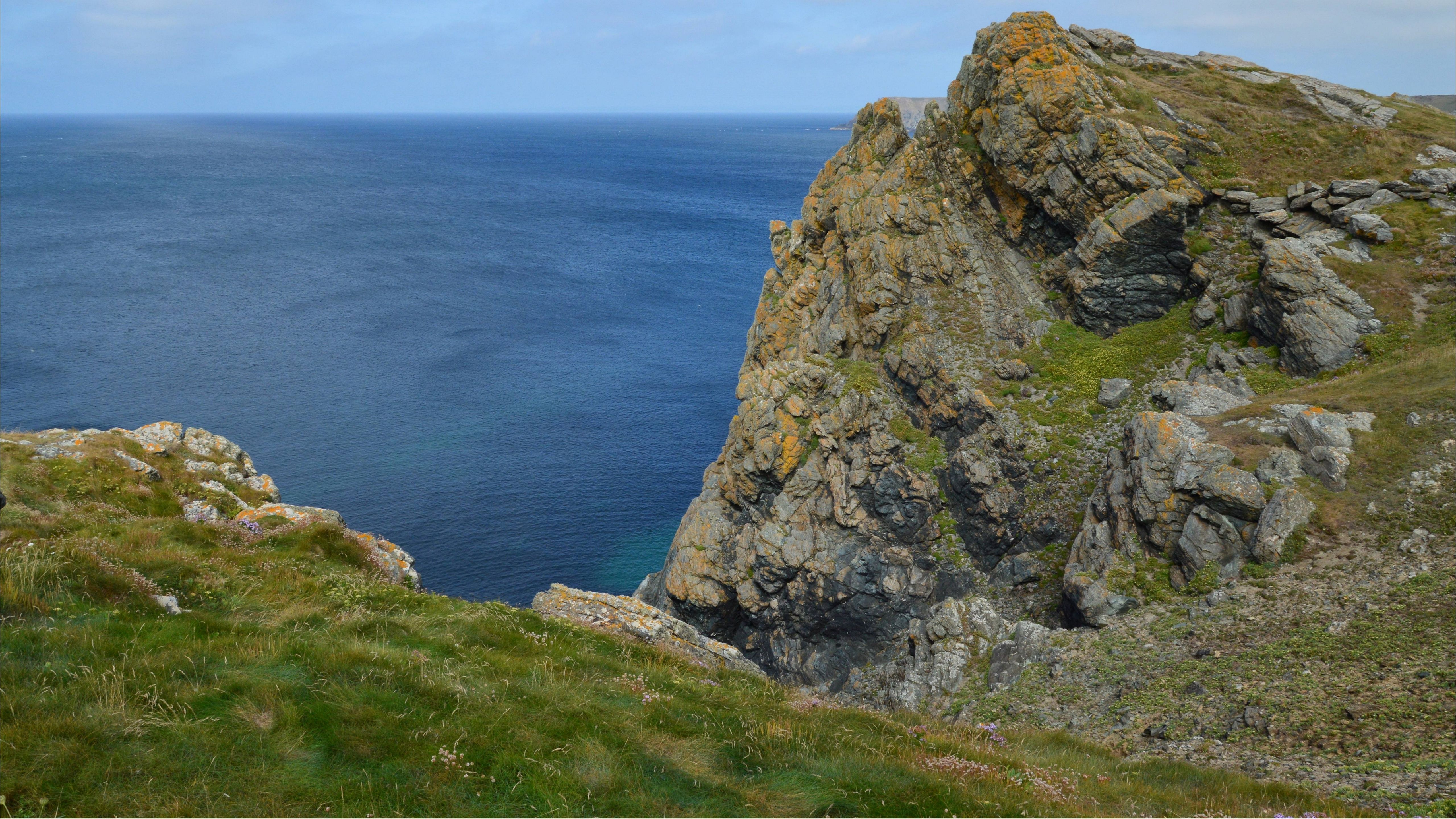 Majestic rocky cliff with vibrant hues overlooking serene ocean waters.