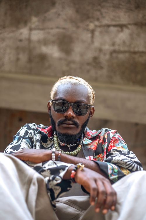 Free Stylish man with trendy accessories sitting casually outdoors in a low-angle shot. Stock Photo