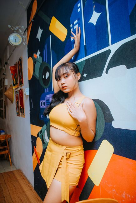 Young woman in yellow outfit posing against a colorful urban art wall indoors.